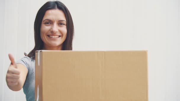 Mujer joven bonita está sosteniendo caja de cartón grande, dando pulgar hacia arriba, sonriendo . — Vídeos de Stock