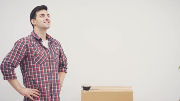 El hombre inspirado está mirando alrededor de su nuevo apartamento, manteniendo las manos akimbo, luego bebiendo café, sonriendo, mirando muy contento . — Vídeo de stock