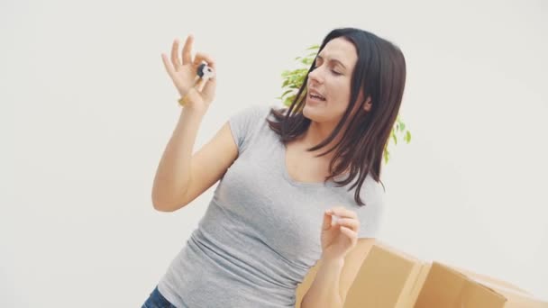 Souriante jeune femme montre les clés de son nouvel appartement, hochant la tête, dansant et agitant joyeusement les mains . — Video