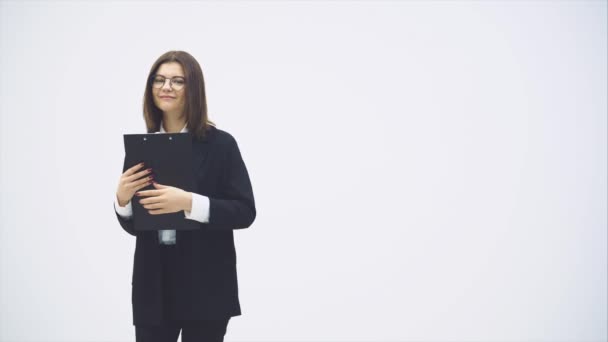 Jolie femme d'affaires en costume noir debout avec porte-papier dans ses mains, posant avec expression de visage heureux . — Video