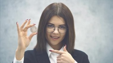 Siyah takım elbiseli, kendine güvenen genç bir iş kadını elinde gümüş bir para tutuyor, parmağıyla işaret ediyor, başını sallıyor, başparmağını sallıyor..