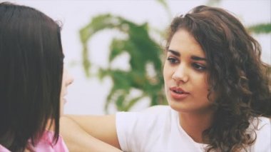 İki kız arkadaş sıcak ev ortamında kanepede oturarak konuşuyorlar. Esmer, beyaz bir kız kameranın karşısında oturuyor, bulanık..