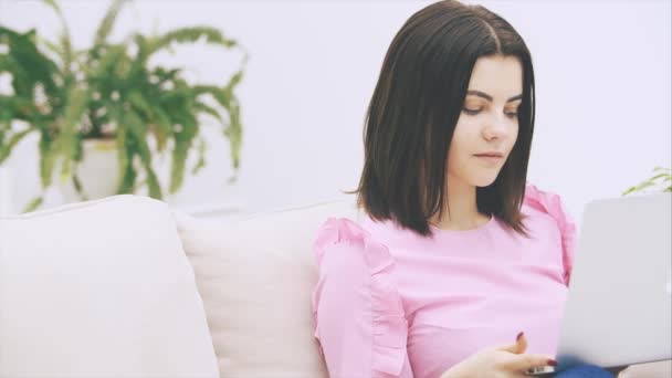 Schattig Kaukasisch brunette meisje zitten op de bank, met laptop, surfen op het internet, reageren op iets emotioneel, op zoek naar zeer opgewonden. — Stockvideo