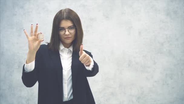 Впевнена молода бізнес-леді в офіційному чорному костюмі тримає срібну монету, віддаючи великий палець . — стокове відео