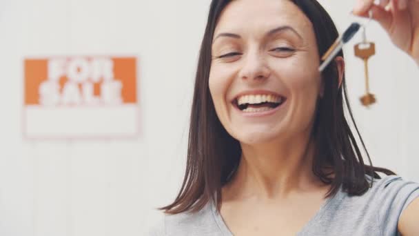 Joven hermosa mujer está sosteniendo las llaves de un nuevo apartamento, sonriendo, dando el pulgar hacia arriba, ofreciendo casa en venta y mudarse . — Vídeo de stock