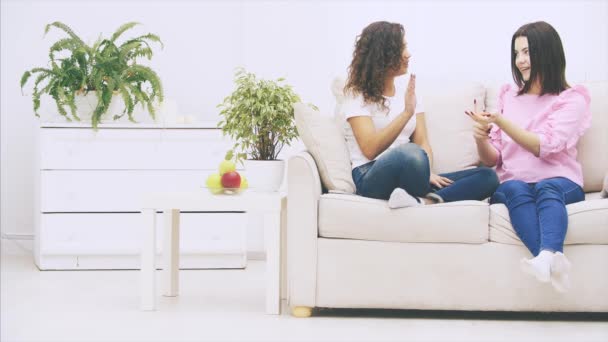 Twee vriendinnen praten zittend op de bank in een warme huiselijke omgeving, geven vijf, glimlachend. — Stockvideo