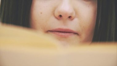 Meraklı genç bayan bir kitap okuyor, tamamen ilgili ve heyecanlı görünüyor. Kamera yukarı çıkıyor..