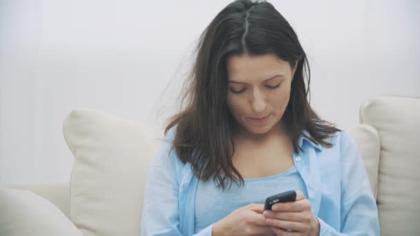 Mujer admirable se concentra en el uso de su teléfono inteligente, mientras está sentado en el sofá, en casa. De cerca. Copiar espacio. 4K . — Vídeo de stock