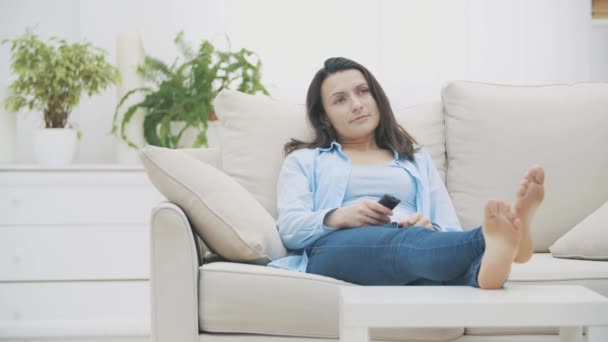 Mujer atractiva se aburre viendo la televisión y bostezos, sentado en el sofá en casa. De repente, grita sobre su emoción. Copiar espacio. 4K . — Vídeo de stock