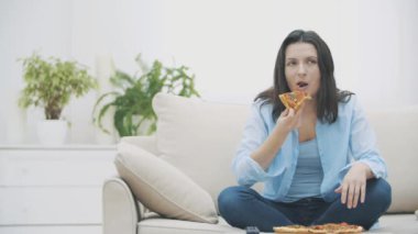 Aç kadın bir kanepede otururken televizyon programını değiştiriyor. O pizza yiyor. 4k.