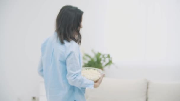 Happy woman tient d'énormes assiettes profondes avec du maïs soufflé et des chips. Elle va s'asseoir sur le canapé. 4K . — Video