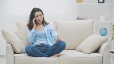 Mavi tişörtlü çekici bir kadın evde otururken telefonla konuşuyor. Ağır çekim. Uzayı kopyala 4k.