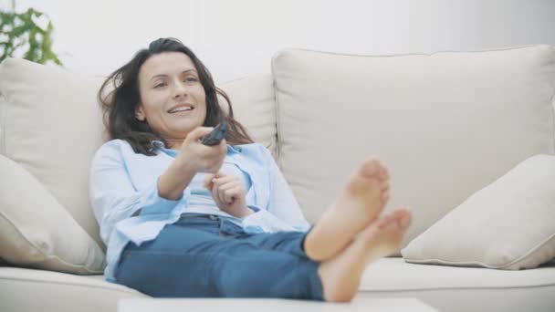 Devagar. Mulher atraente está entediado por assistir TV, sentado no sofá em casa. Espaço para cópia. 4K . — Vídeo de Stock