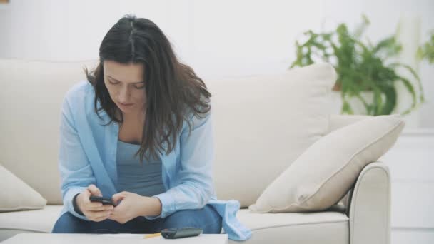 칭찬 할 만 한 여성은 집에서 소파에 앉아 스마트폰을 사용하는 데 집중 한다. 느린 동작. 복사 공간. 4k. — 비디오