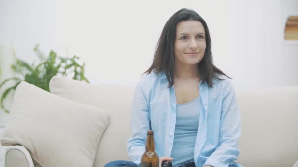 Медленно. Молодая женщина сидит на диване, ест пиццу и пьет пиво. Вкуснятина. 4K . — стоковое видео