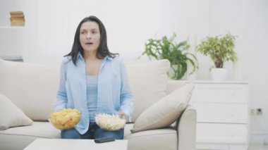 Yavaş ol. Mutlu kadın elinde patlamış mısır ve cips dolu kocaman tabaklar tutuyor. Odak noktasından çıkıyor. 4k.
