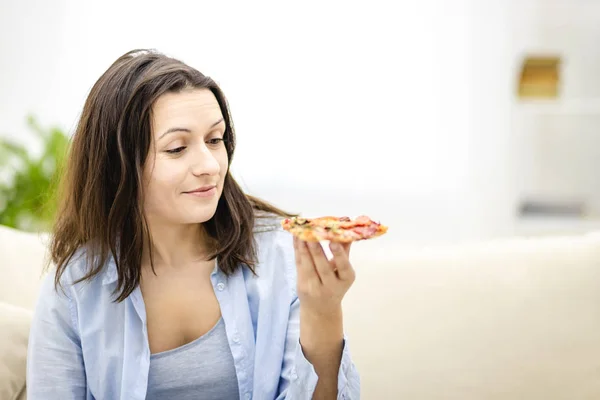 Mooi meisje kijkt naar pizza plakje, op een lichte achtergrond. Sluit maar af. Kopieerruimte. — Stockfoto