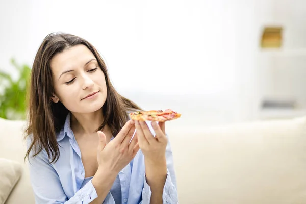 Mooi meisje is op zoek naar pizza slice en glimlacht breed, op lichte achtergrond. Sluit maar af. Kopieerruimte. — Stockfoto