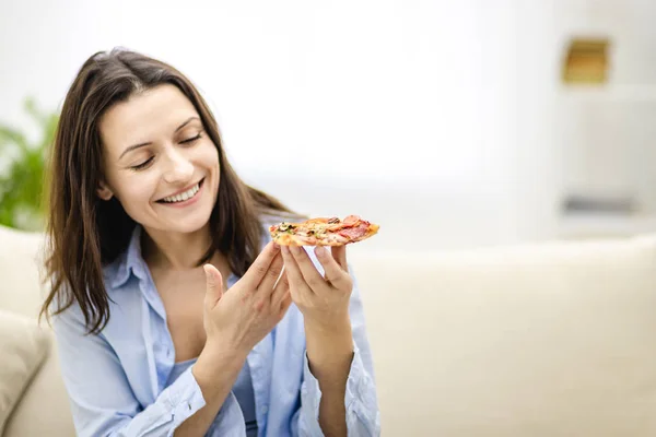 Gyönyörű lány néz pizza szelet és mosolyog széles körben, könnyű háttérrel. Közelről. Fénymásolási hely. — Stock Fotó