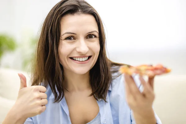 Mujer agradable es sonríe ampliamente, sobre fondo claro. La mujer está mostrando su dedo pulgar hacia arriba, sosteniendo una rebanada de deliciosa pizza. De cerca. . — Foto de Stock