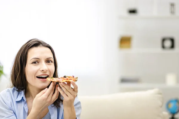 Attractive brunette woman is looking at straight at the camera. She wants to eat pizza slice and smiles widely, on light background. Close up. Copy space. — Stock Photo, Image