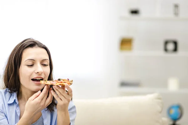 Mujer morena atractiva quiere comer rebanada de pizza, mirándolo, sobre un fondo claro. De cerca. Copiar espacio . — Foto de Stock