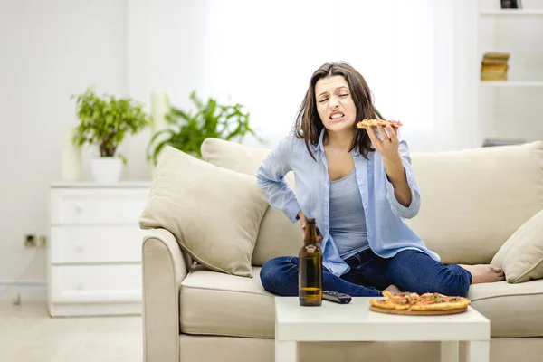 Donna bruna tiene una fetta di pizza. Ha mal di stomaco. Una donna ha mangiato troppo. Copia spazio . — Foto Stock