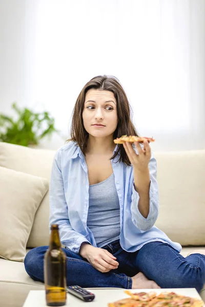 Mujer morena mira una rebanada de pizza con asco. Difícil elección . —  Fotos de Stock