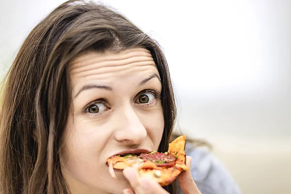 Attraktive brünette Frau will Pizza-Scheibe essen, sieht es, auf hellem Hintergrund. Nahaufnahme. Kopierraum. — Stockfoto