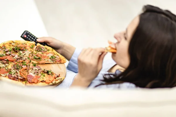 Növény. Csinos nő otthon fekszik a kanapén, és tévét néz, miközben pizzát eszik. Felülnézet. — Stock Fotó