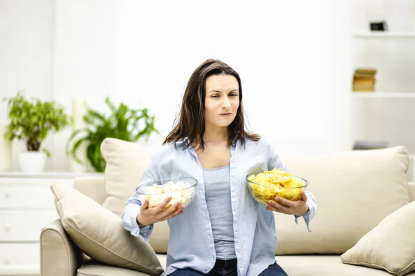 Mujer codiciosa está tratando de elegir entre maíz pop y patatas fritas. Ella eligió ambos, y no quiere compartir . — Foto de Stock