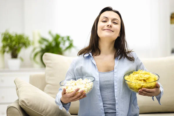 Mujer feliz y complacido sostiene platos profundos con maíz pop y patatas fritas. Ella está lista para filmar viendo . — Foto de Stock