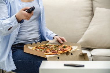 Ekin. Tanınmayan bir kadın evdeki kanepesinde oturuyor ve pizza yerken televizyon izliyor. Boşluğu kopyala.