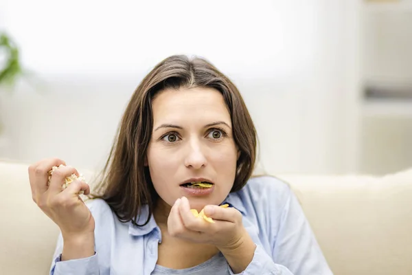 De vrouw doet haar mond open, verbaasd. Ze houdt twee handvol snacks vast: chips en popcorn. Sluiten.. — Stockfoto