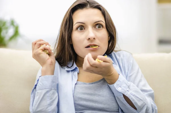 La mujer abre la boca, asombrada. Ella sostiene dos puñados de bocadillos: papas fritas y maíz pop. De cerca. . —  Fotos de Stock