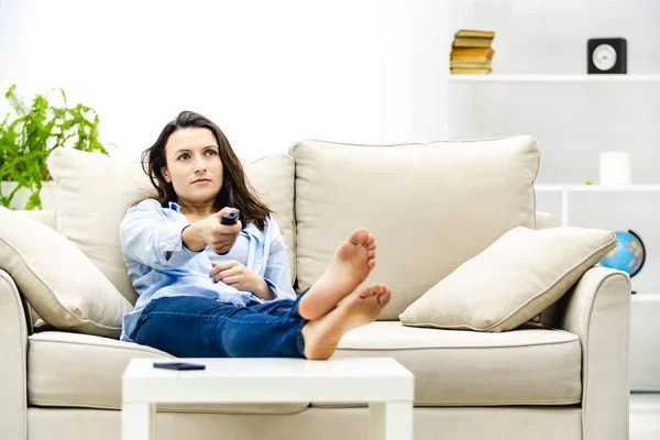 Jovem concentrada está assistindo TV, sentada em um sofá. Espaço de cópia . — Fotografia de Stock