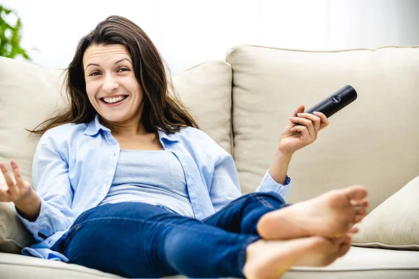 Glückliche junge Frau sitzt auf einem Sofa vor dem Fernseher. Sie lächelt breit. Kopierraum. — Stockfoto