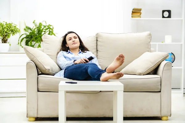 Gelangweilte und entspannte Frau sieht fern, auf einem Sofa liegend. Kopierraum. — Stockfoto
