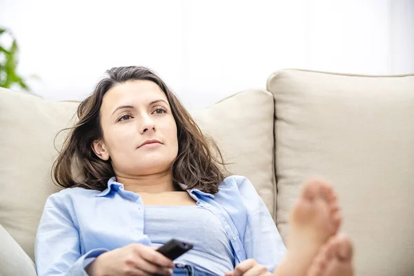 Uprawa. Znudzona i zrelaksowana kobieta ogląda telewizję, leżącą na kanapie. Zamknij się.. — Zdjęcie stockowe