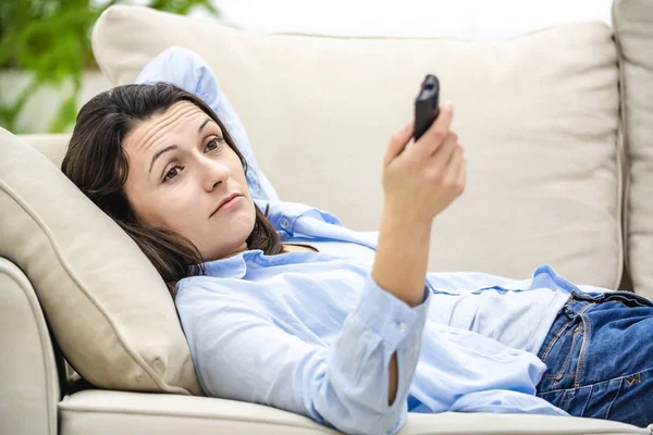 Ernte. Gelangweilte und entspannte Frau sieht fern, auf einem Sofa liegend. Nahaufnahme. — Stockfoto