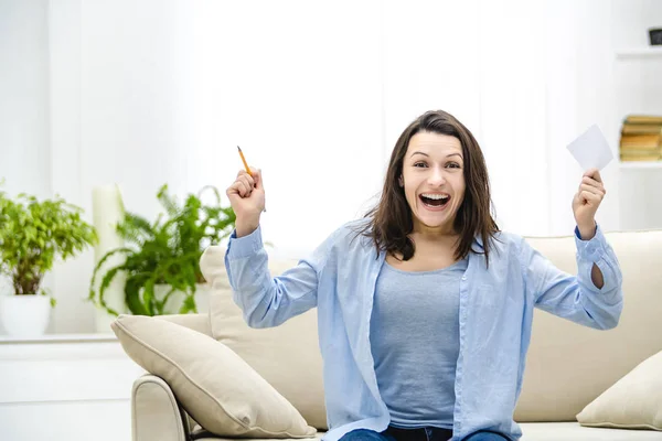 Young woman rejoices sitting on sofa, she won a price. Close up.