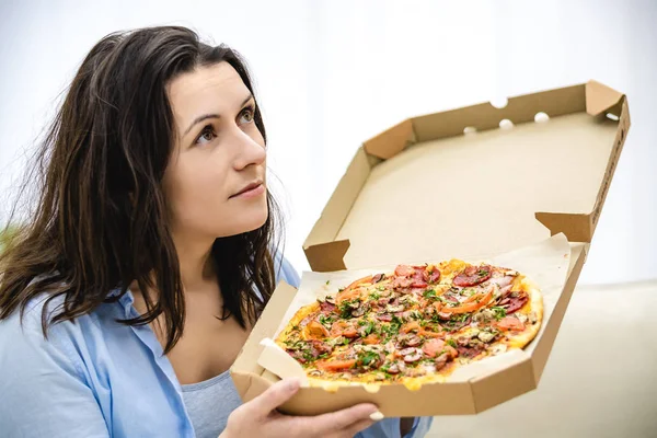 Joven morena mira a un lado y sostiene una pizza caliente en una caja. Copiar espacio. De cerca.  . —  Fotos de Stock