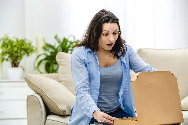 Brunett kvinna öppnar pizzalådan, isolerad, sitter på lätt soffa. — Stockfoto