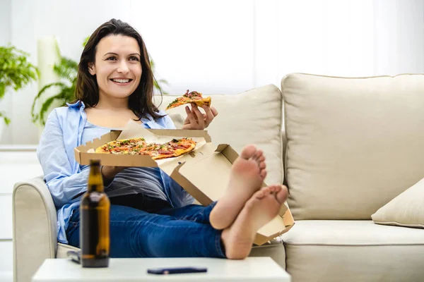 Donna bella e felice sta mangiando la pizza. Sorride sinceramente, seduta sul divano. Copia spazio . — Foto Stock