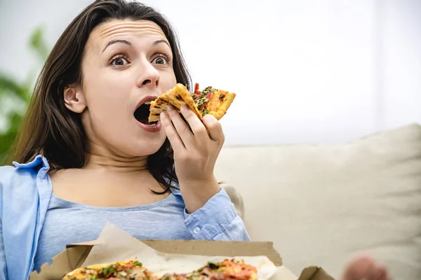 Una donna stupita con le sopracciglia alzate morde una fetta di pizza. Da vicino. . — Foto Stock