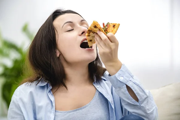 Die schöne junge Frau mit den dunklen Haaren beißt in eine Scheibe heiße Pizza. Kopierraum. Nahaufnahme. — Stockfoto