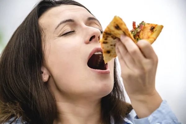 Die schöne junge Frau mit den dunklen Haaren beißt in eine Scheibe heiße Pizza. Kopierraum. Nahaufnahme. — Stockfoto