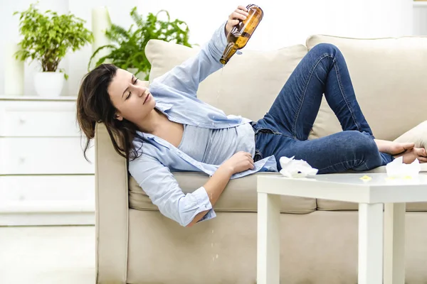 Mujer joven borracha está acostada en el sofá y mirando a la botella vacía. Ella quiere más. . —  Fotos de Stock