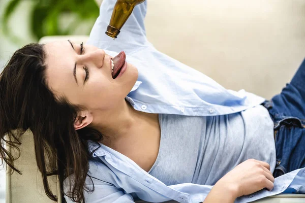 Brunette woman is laying on the sofa and trying to taste the last drop of beer. Close up. — Stock Photo, Image