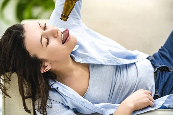 Mujer morena está acostada en el sofá y tratando de probar la última gota de cerveza. De cerca. . — Foto de Stock